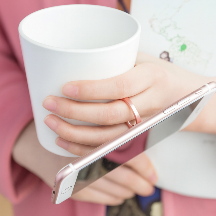 Person holding a white mug and a smartphone with a pink case.