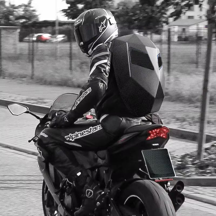 Person riding a motorcycle with a large black backpack on a road.