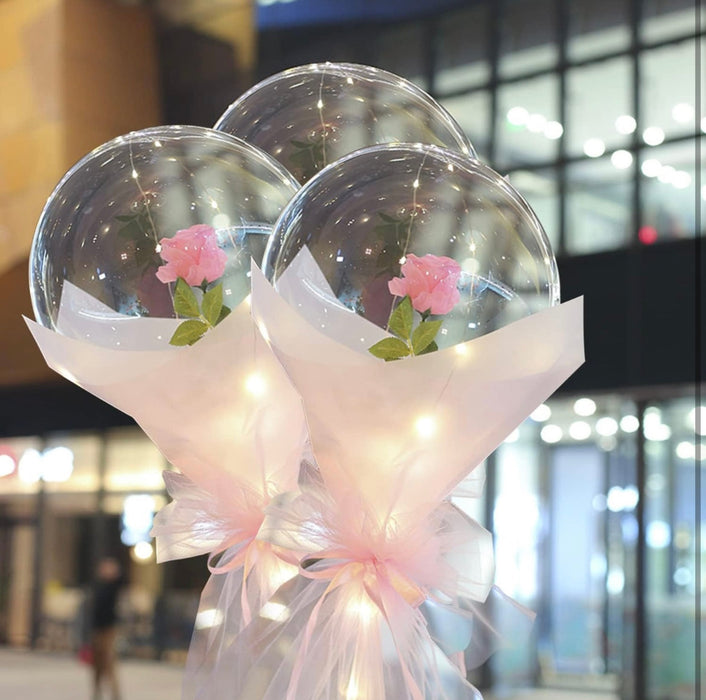 Two transparent bubble balloons with pink flowers and ribbons against a blurred indoor background