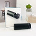 Black cylindrical device with digital display on a white surface, with a mirror reflecting the device.