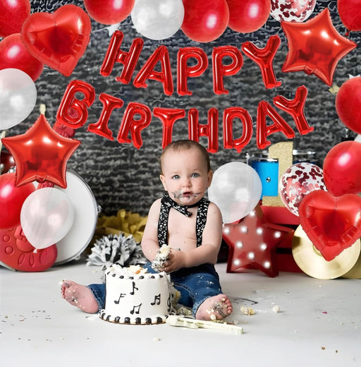 Baby celebrating a birthday with balloons and a cake, sitting on the floor.