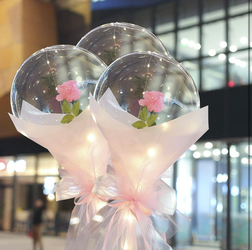 Two transparent bubble balloons with pink flowers and ribbons against a blurred indoor background