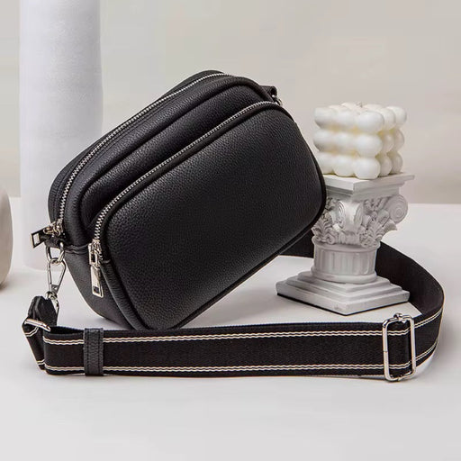 Black leather crossbody bag with a strap on a light background